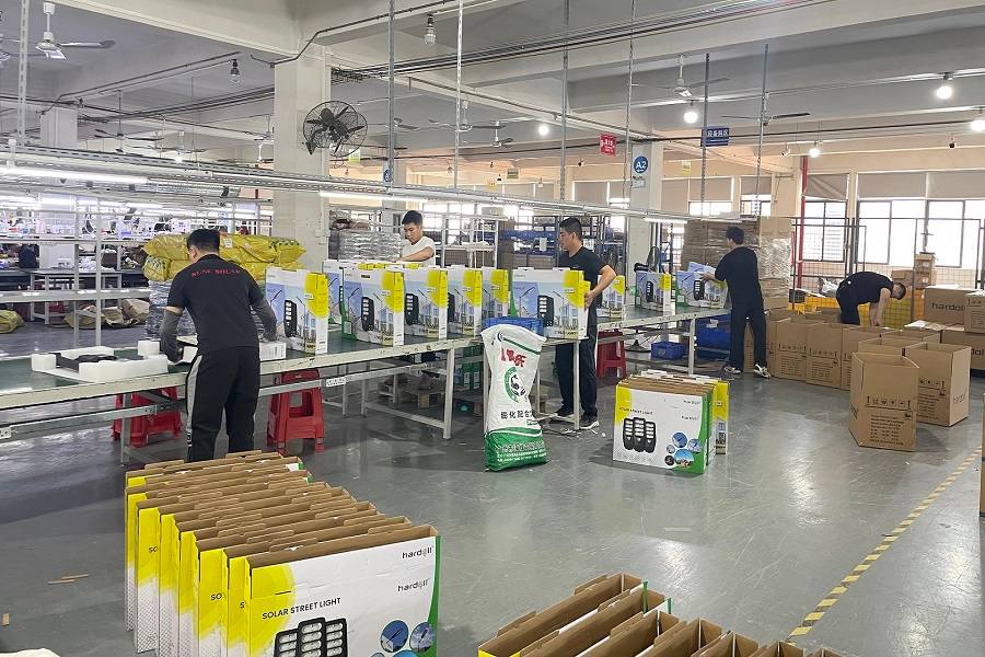 Workers assembling and packaging commercial solar street lights along an ISO9001 factory production line.