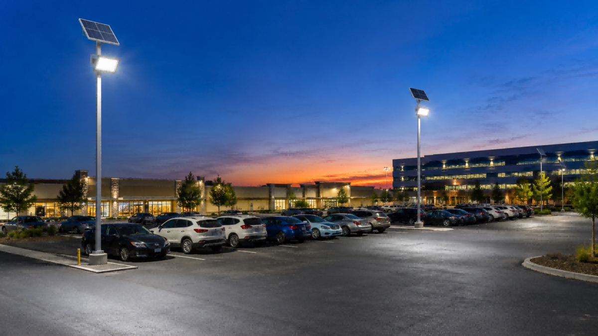 High-mast commercial solar flood lights illuminating a retail parking lot and access corridor using Quasar QSKZ-AL-2835 fixtures.