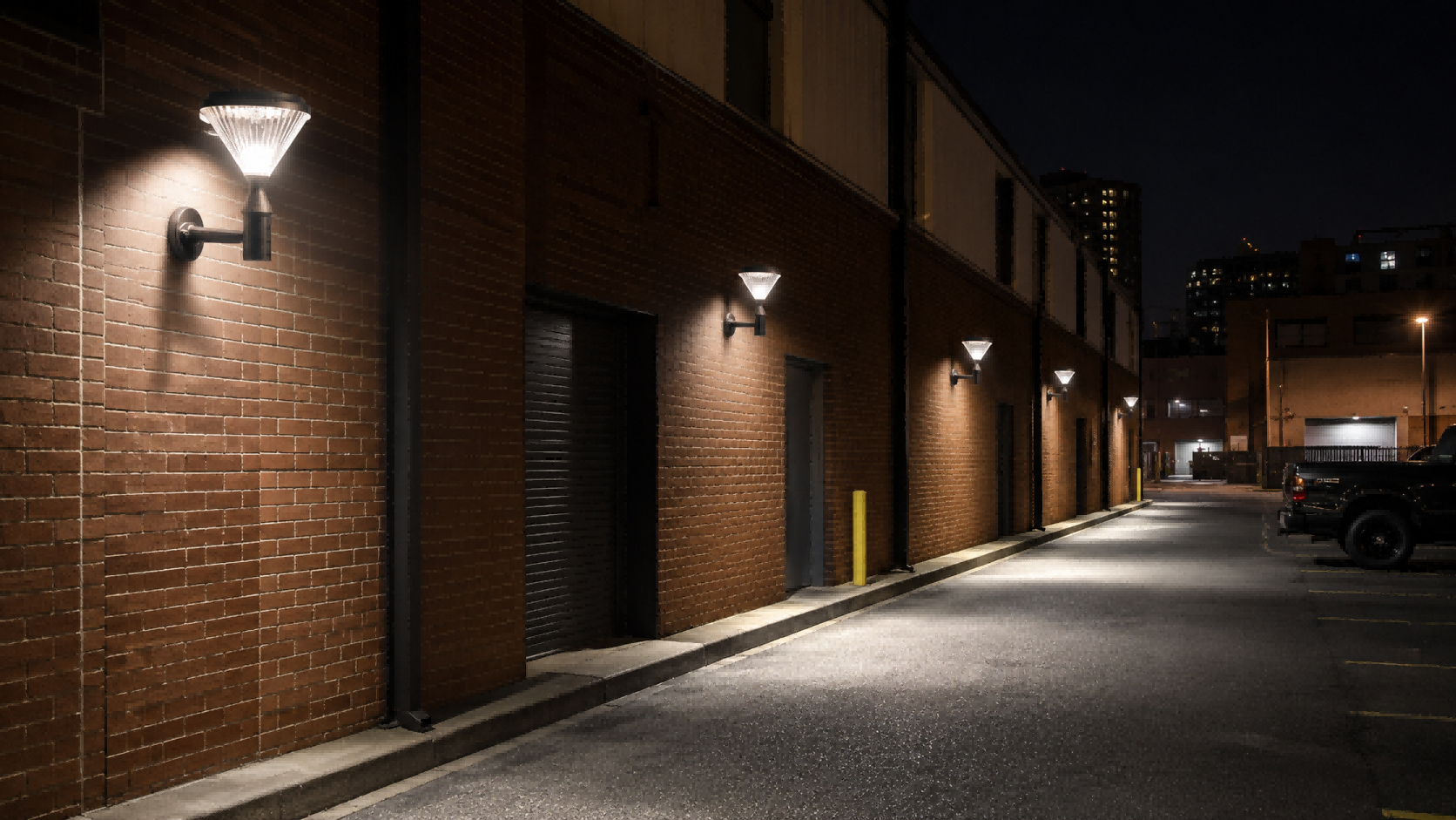 Solar wall-pack lights mounted on brick facility walls illuminating an outdoor service driveway and vehicular lane at night.