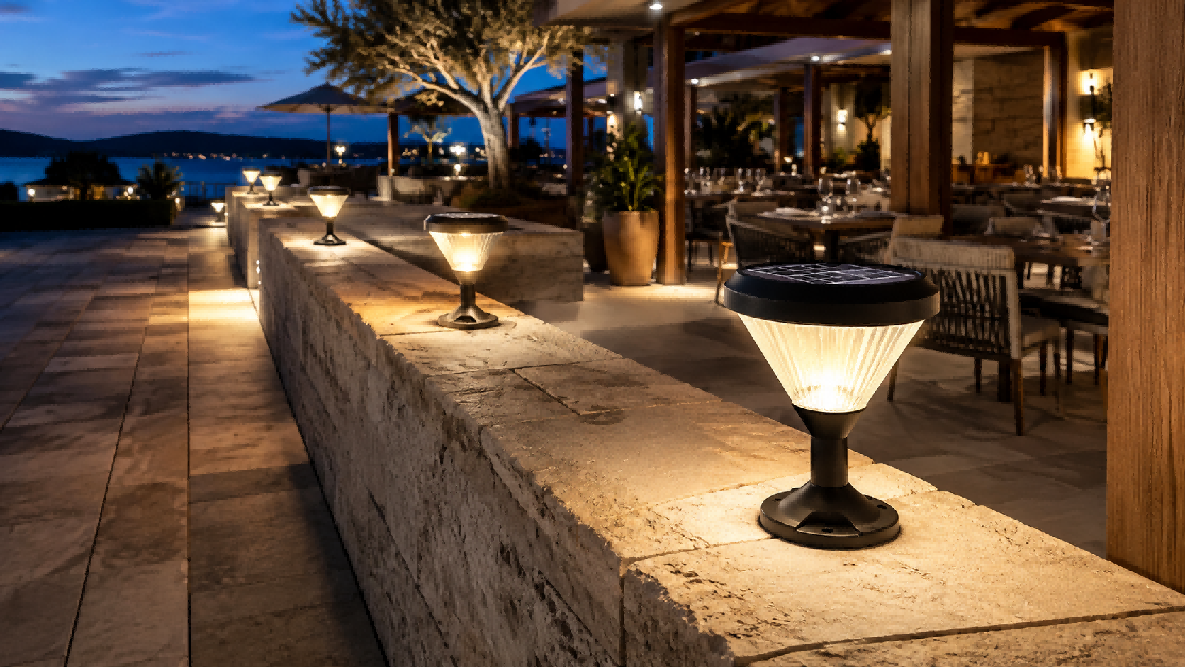 Compact solar mini pillar light with diamond optical diffuser bolt-mounted on a stone masonry wall ledge along a luxury resort patio terrace at dusk.